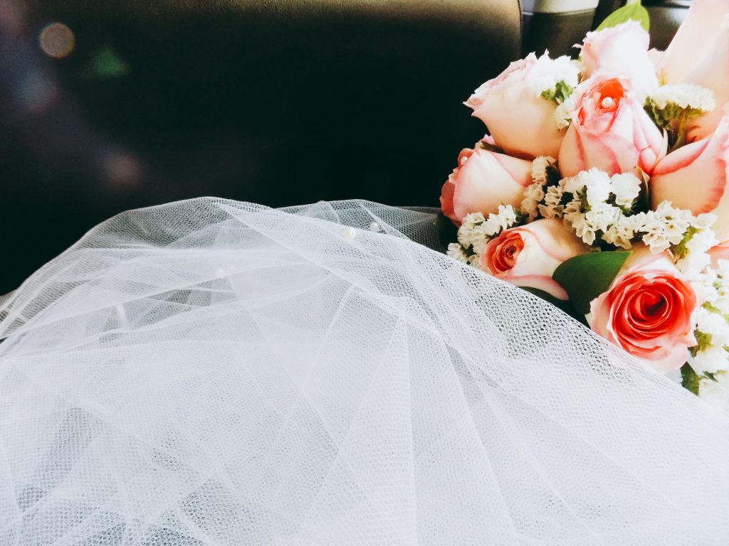 A bouquet of pink roses next to a bride's veil.