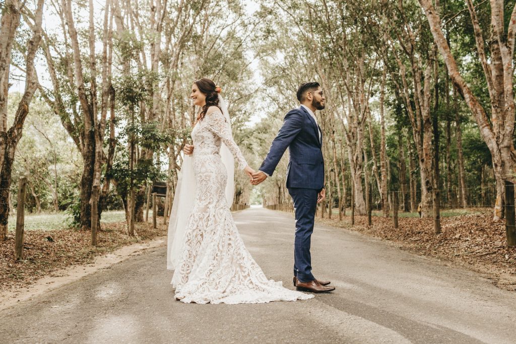 A bride and groom stand back-to-back holding hands.