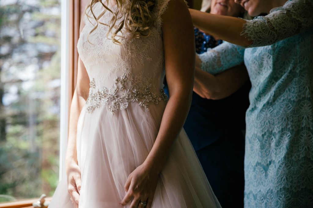 Two women help button a bride's wedding dress.