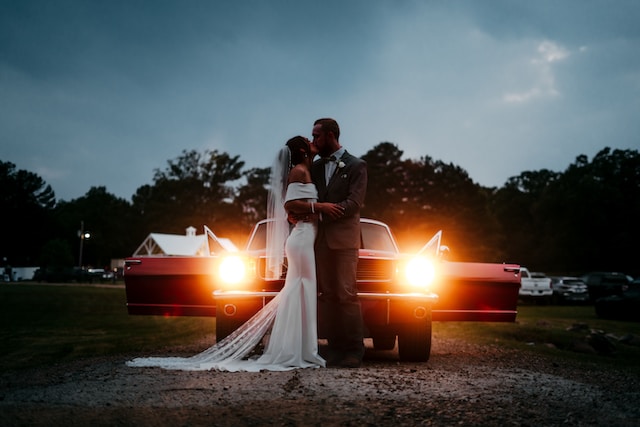 A bride and groom stand in front of their getaway car.