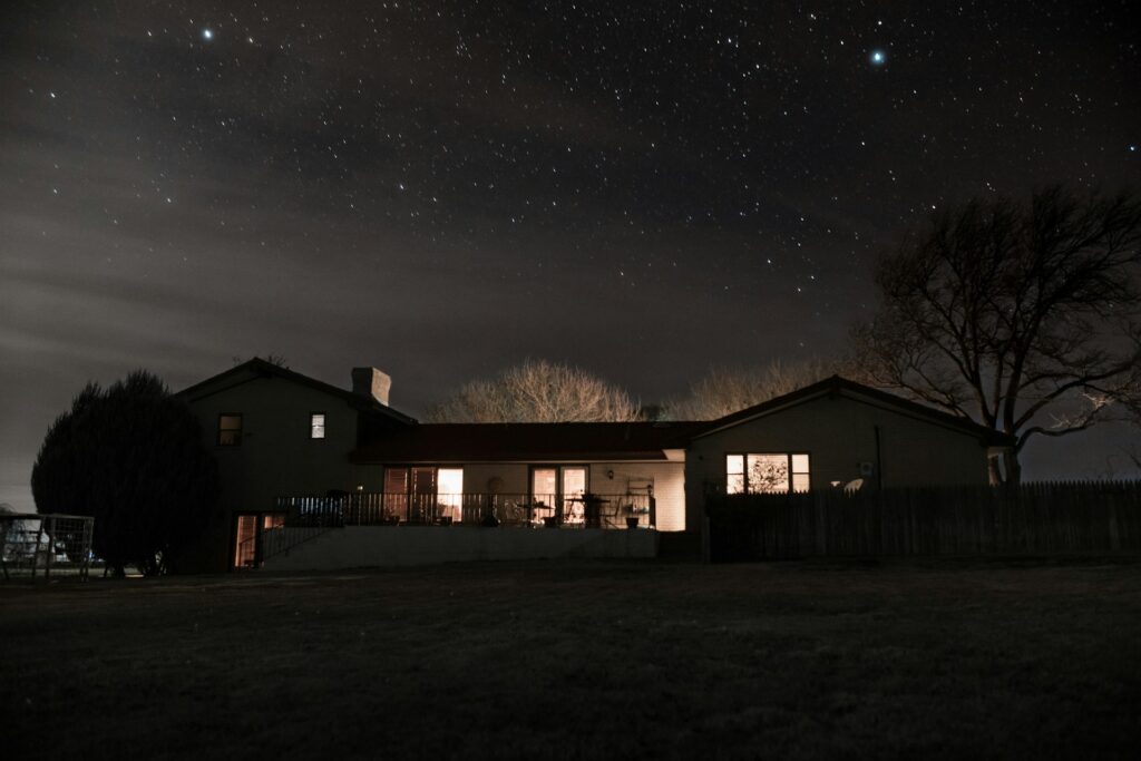 A house sits under a starry sky at night. The internal lights are all one, which is one of the best home security tips for women who live alone.