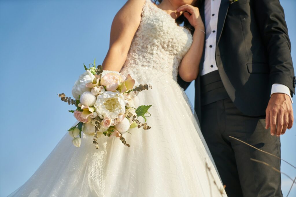 The bride and groom pose in a grassy area, radiating joy in their wedding outfits, surrounded by nature.