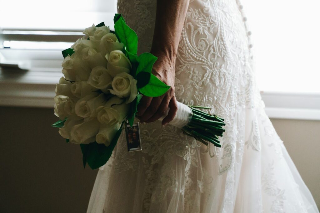 A bride wearing an embroided wedding gown gracefully holds a bouquet of white roses, embodying elegance and romance on her special day.
