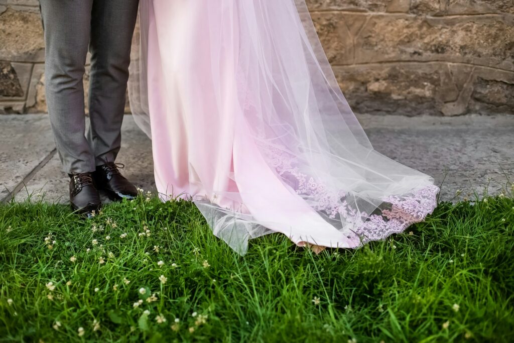 A bride in a light pink gown and a groom in a suit stand together against a charming stone wall