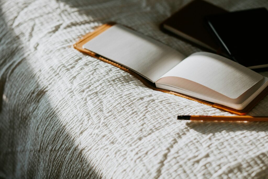 an open book sitting on top of a bed next to a pencil, journaling is one of the most popular analog hobbies