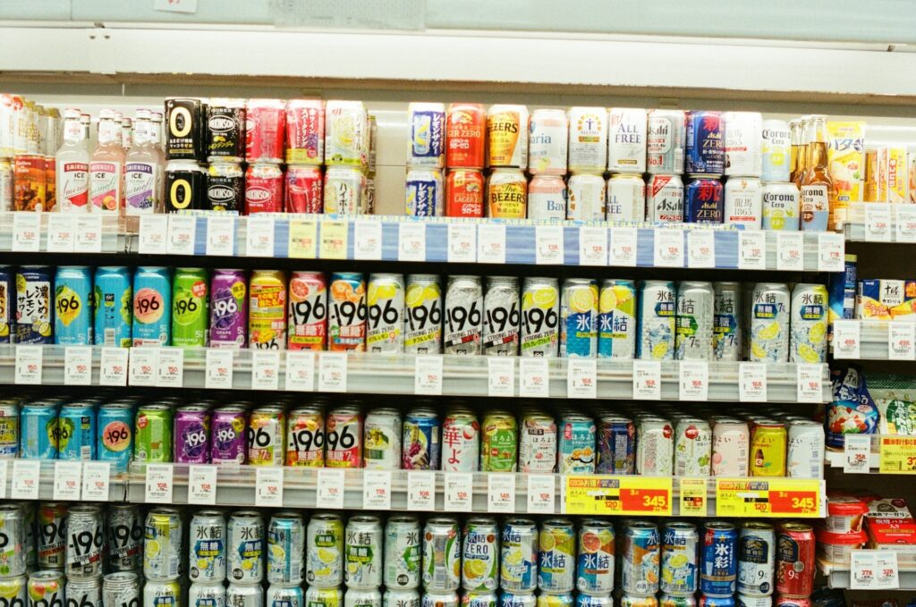 A supermarket shelf filled with various canned drinks, arranged in rows. Bright, colorful labels with diverse designs create a vibrant, busy atmosphere.
