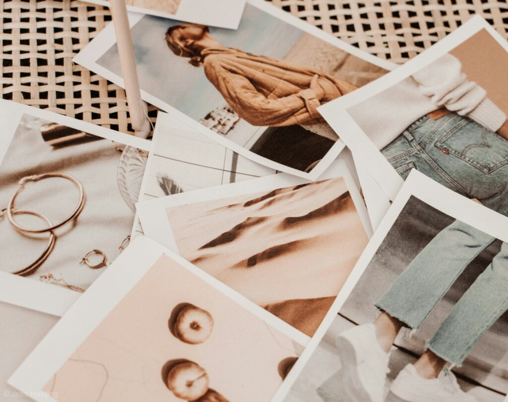 A scattered collection of photographs on a wicker surface shows jewelry, fashion outfits, and landscapes, conveying a relaxed, artistic vibe.