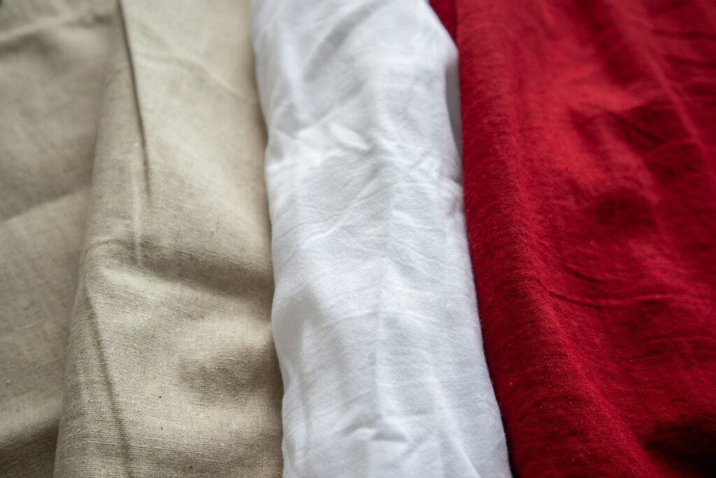 Three folded fabric pieces in beige, white, and red lay side by side, showcasing their textures. The image conveys a sense of softness and warmth.
