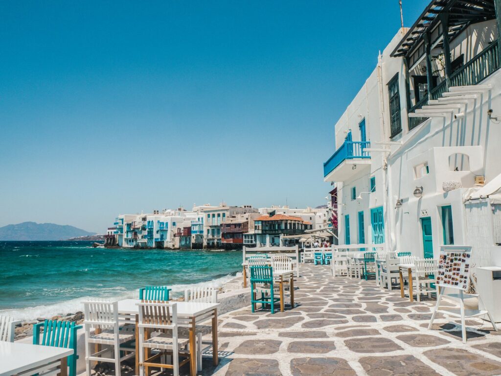 A sidewalk running alongside water and white and blue buildings on a Greek Island