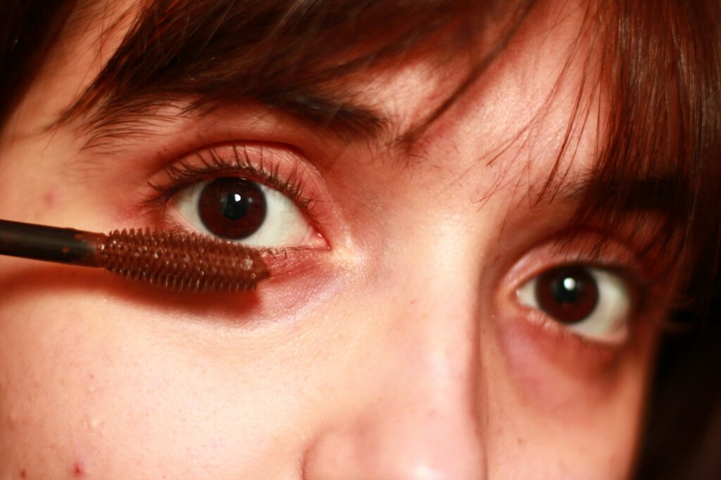 A closeup of a woman with brown eyes putting on brown mascara
