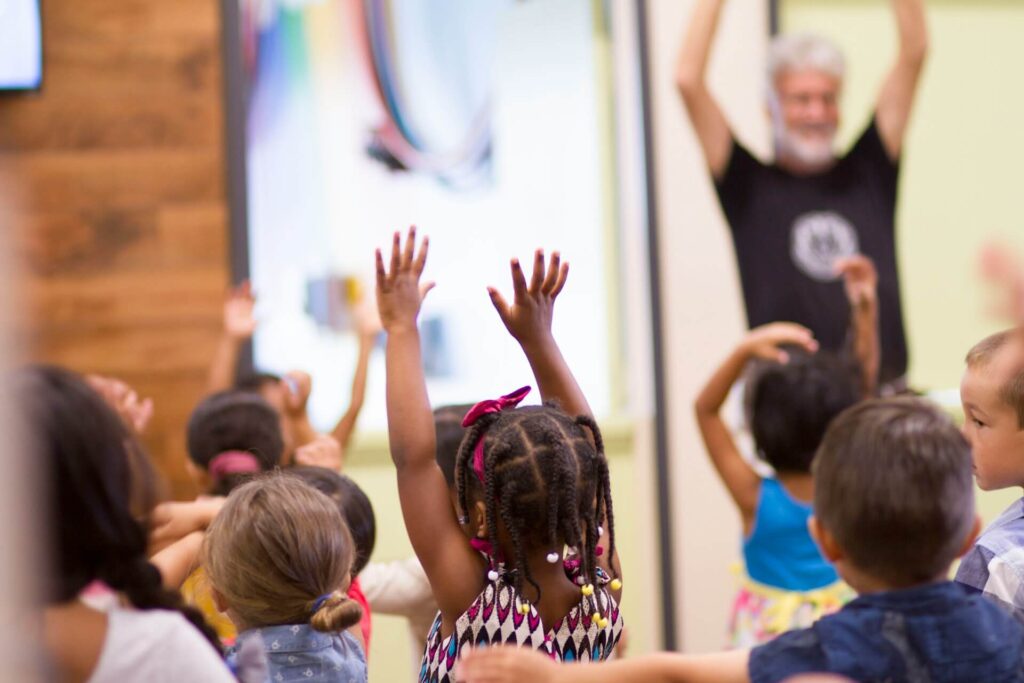 Elementary school students eagerly raising their hands in a bright classroom