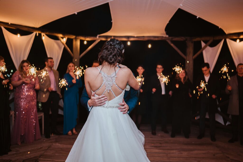 Wedding guests holding sparklers around kissing bride and groom