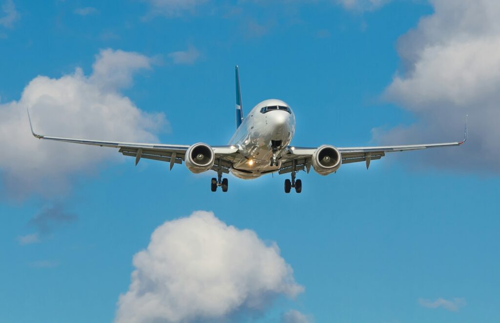 Commercial airplane flying towards the camera against a blue sky with scattered clouds. The landing gear is visible, conveying approach for landing.
