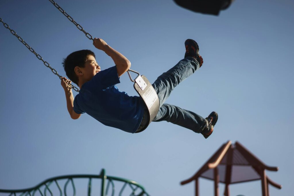 Young child smiling and laughing while swinging on a playground swing
