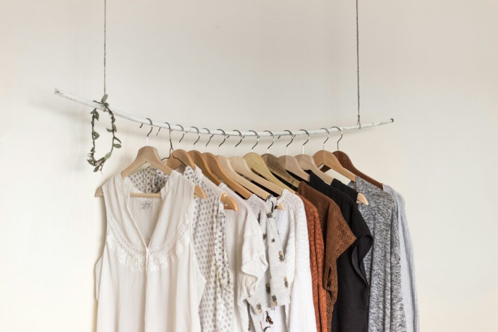 Aesthetic display of clothing on wooden hangers, featuring light, earth-toned dresses and tops on a minimalist white branch, set against a plain wall.