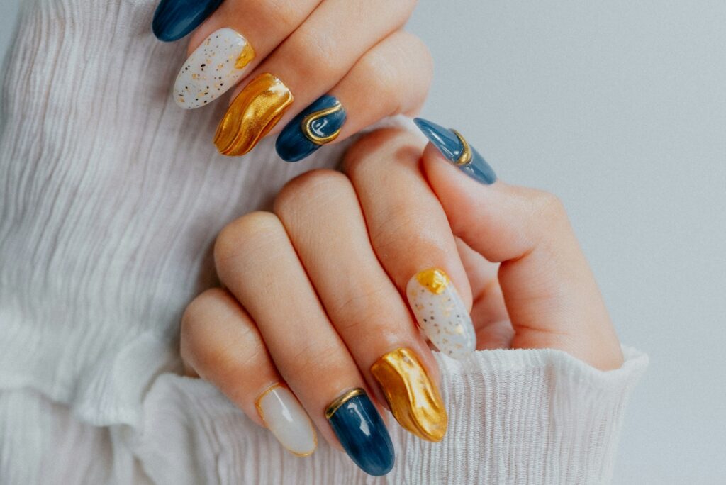 Close-up shot of hands with blue and gold nail art, featuring glossy finishes, speckled patterns,