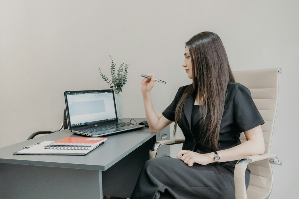 A woman at a desk, engaged with her laptop, surrounded by office supplies and a plant.