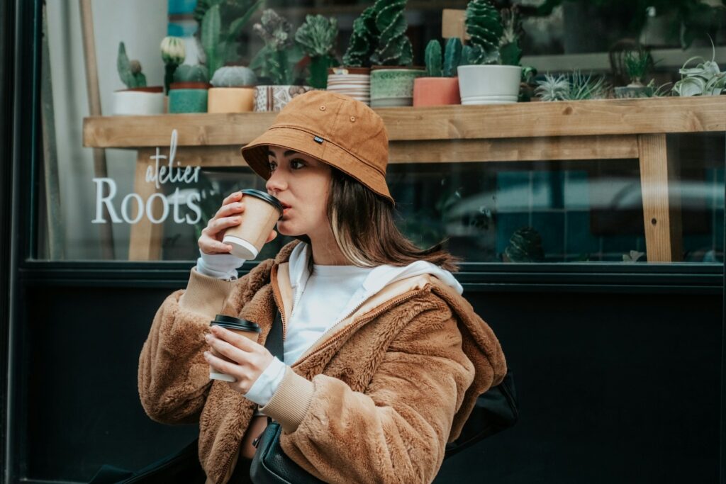 A woman in a stylish hat sips coffee at an outdoor café, surrounded by a vibrant street scene.