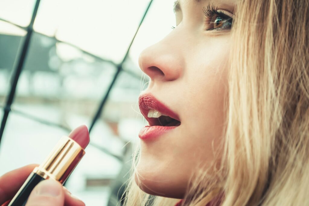 A woman with blonde hair is about to reapply a soft, pink lipstick