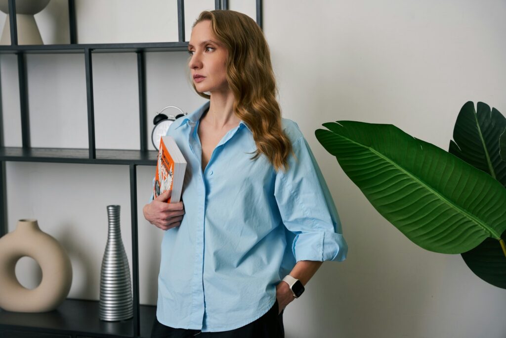 A woman wearing a blue shirt poses next to a lush green plant in a well-lit room.