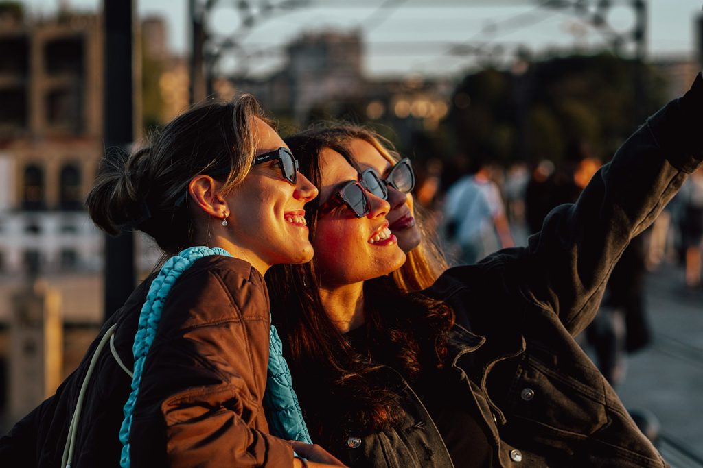 Three women smiling and posing together while taking a selfie with a camera.