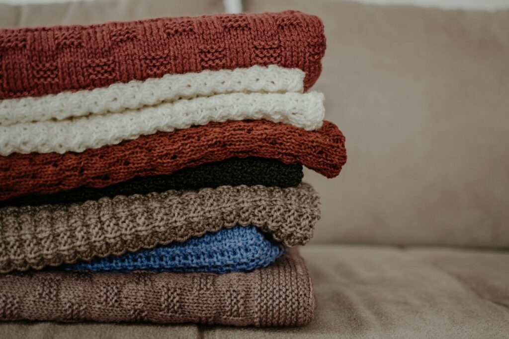Stack of woven knit blankets and pillows layered on a couch for cozy, folk-inspired texture