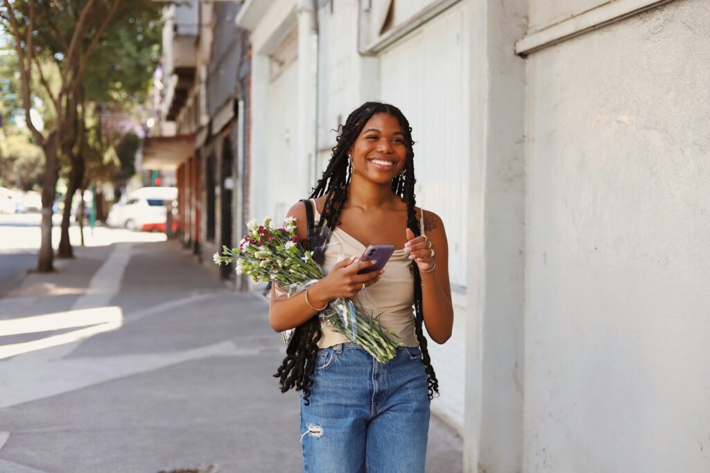 woman smiling while walking with a flower bouquet and holding a phone