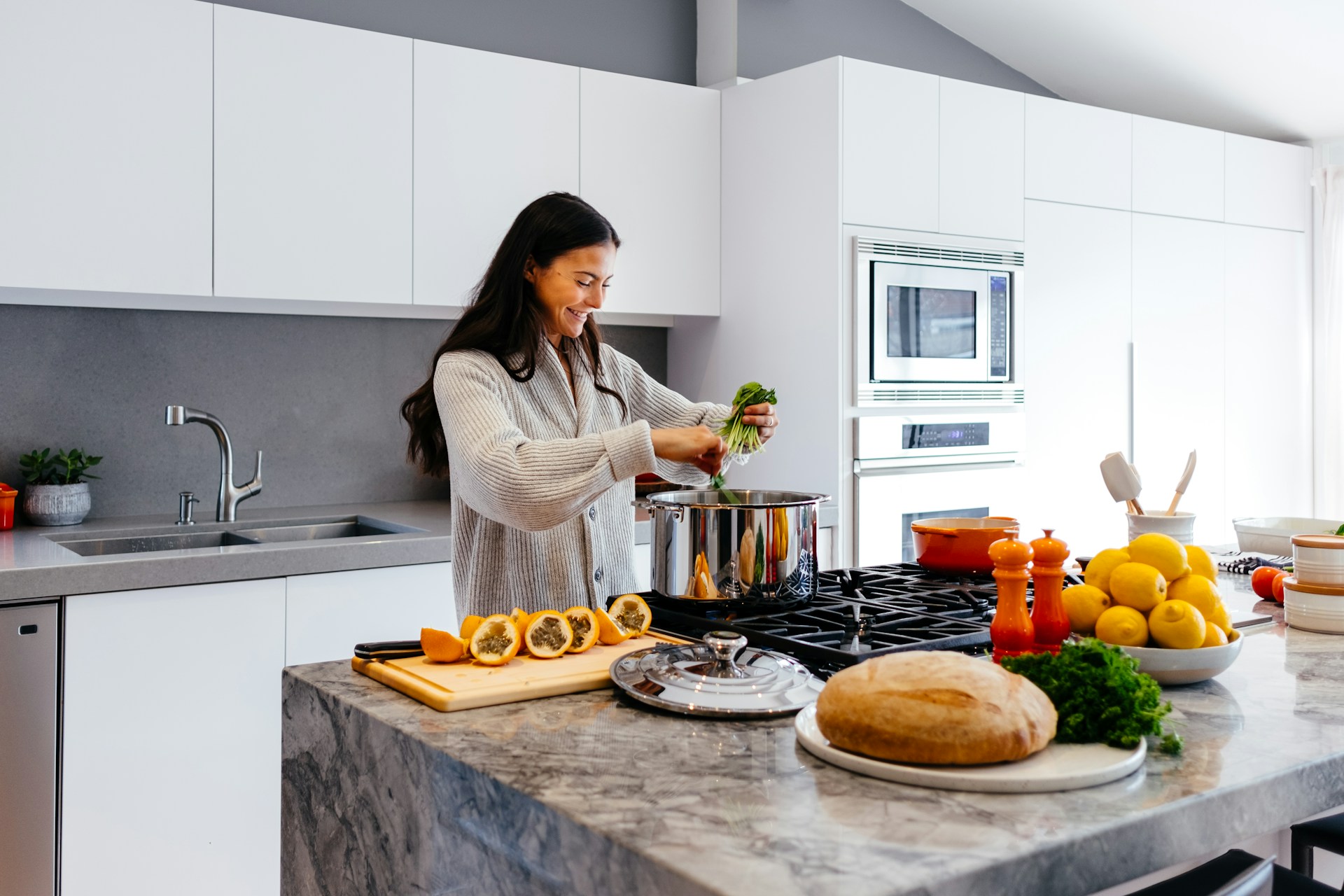 A woman prepares a variety of dishes in a well-equipped kitchen filled with fresh ingredients and cooking utensils.