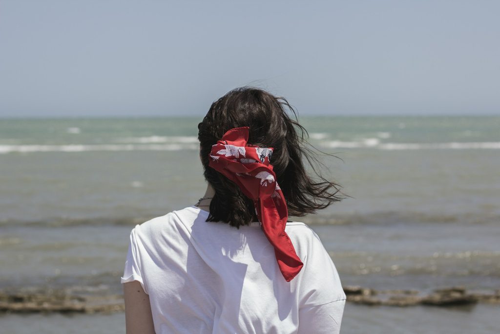 Woman standing in front of the ocean with silk bandana tying her hair