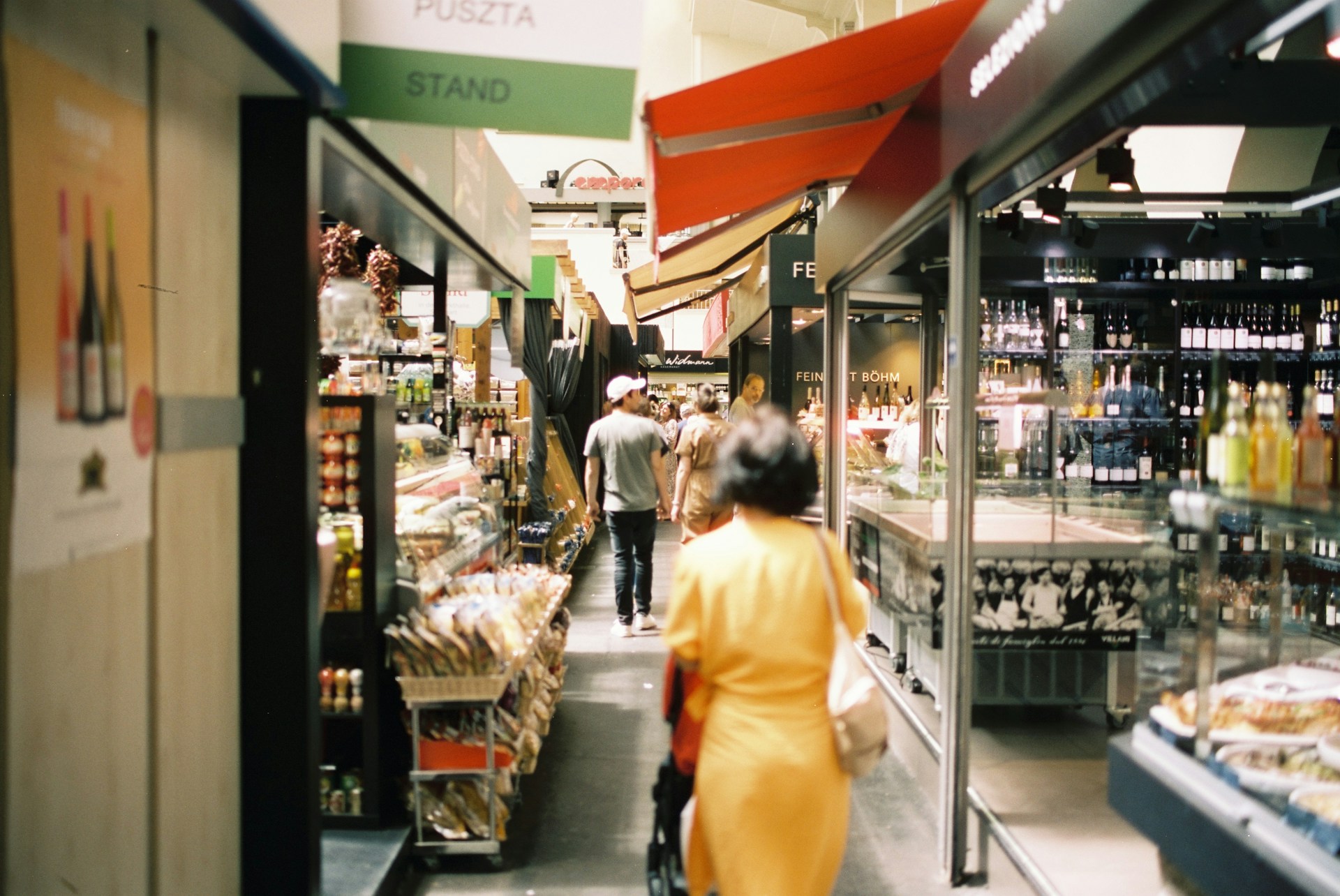 A woman in a yellow dress walking down a narrow aisle, surrounded by shelves filled with various items on both sides.