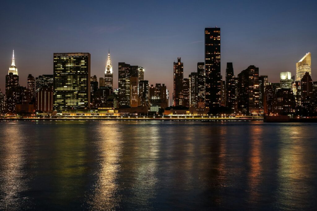 City skyline lit up at night, reflecting across the water