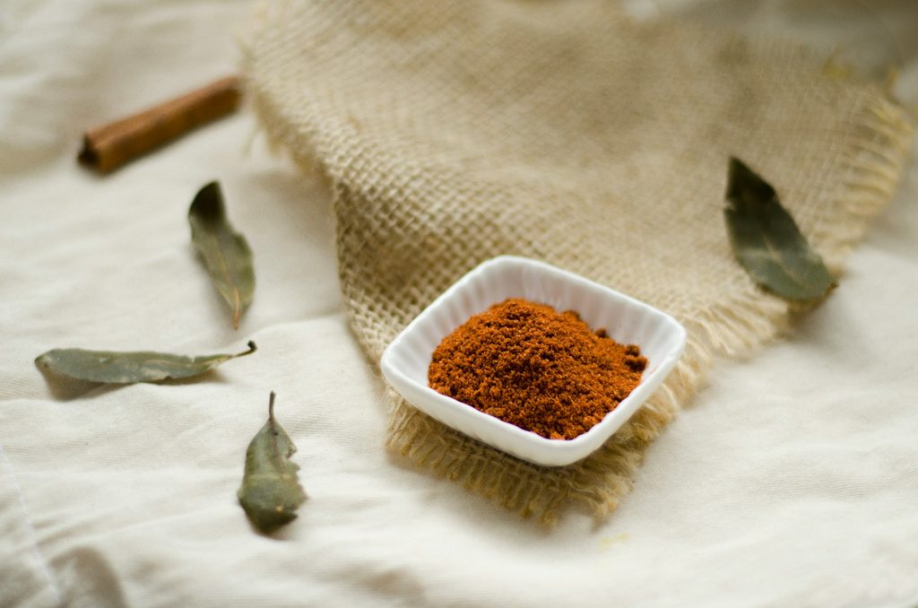 Small bowl of pumpkin spices on white table cloth with beige towel and dried leaves