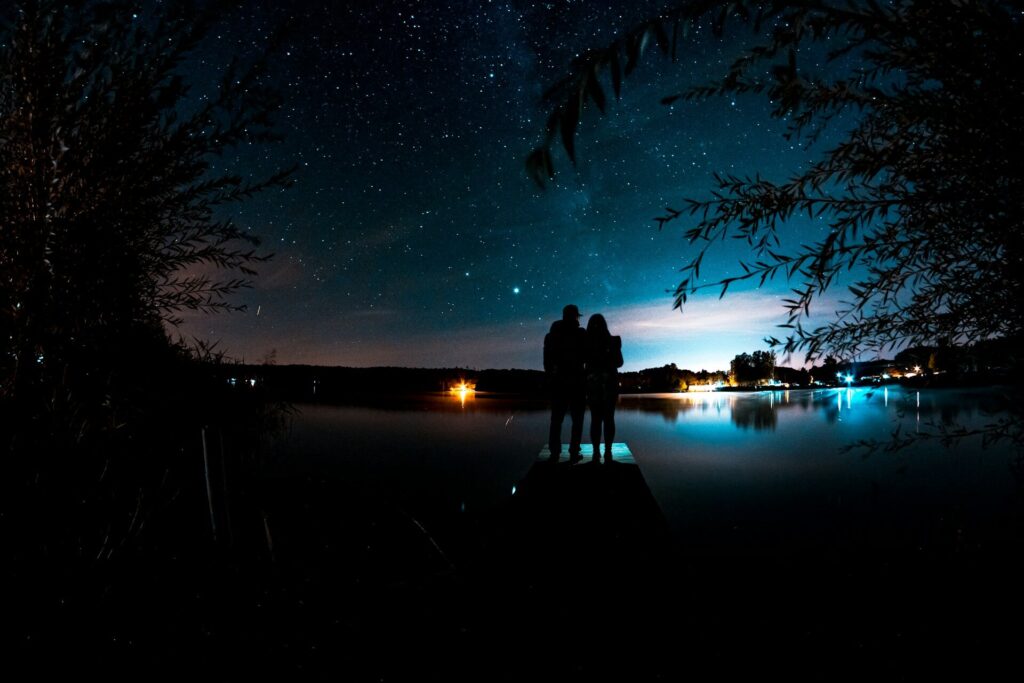Silhouette of a couple standing on a dock at night under a starry sky