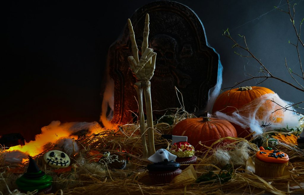 Decorated table with skeleton hand, pumpkins, hay and Halloween food ideas for party
