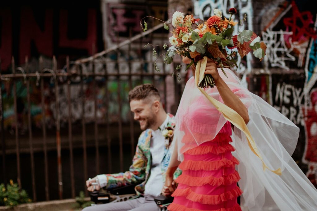 A bride wearing a pink dress and a groom in a wheelchair wearing a floral suit. 