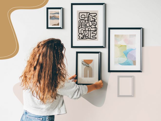 A woman with curly hair adds a picture with a black frame to her gallery wall, one of the easiest ways to decorate your walls.