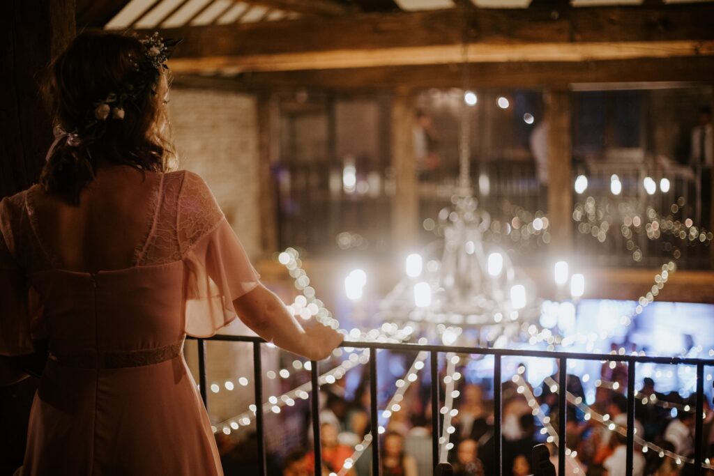 A woman in a pink bridesmaid dress looks over a railing at a wedding reception.