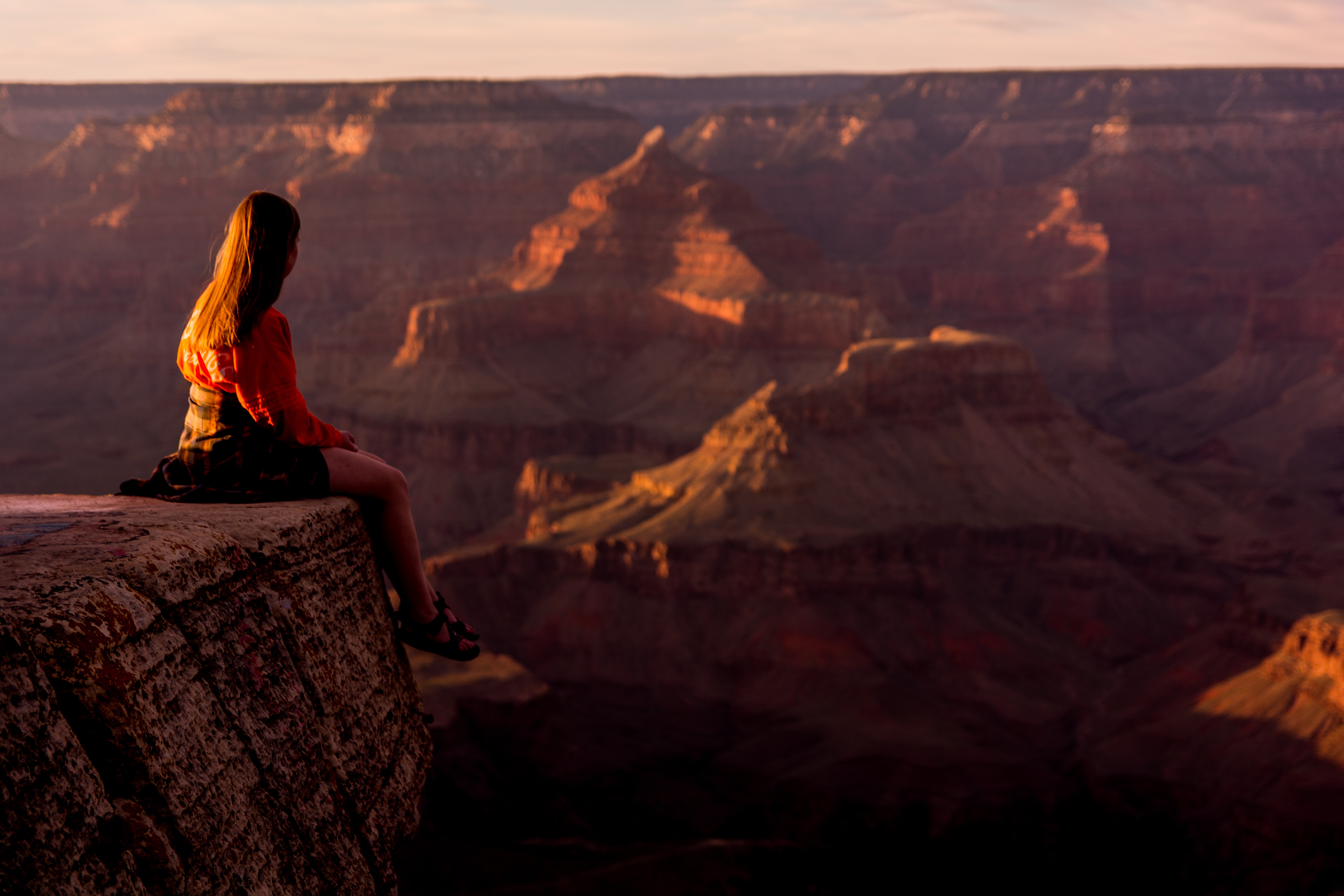 A woman sits on a ledge overlooking the Grand Canyon.