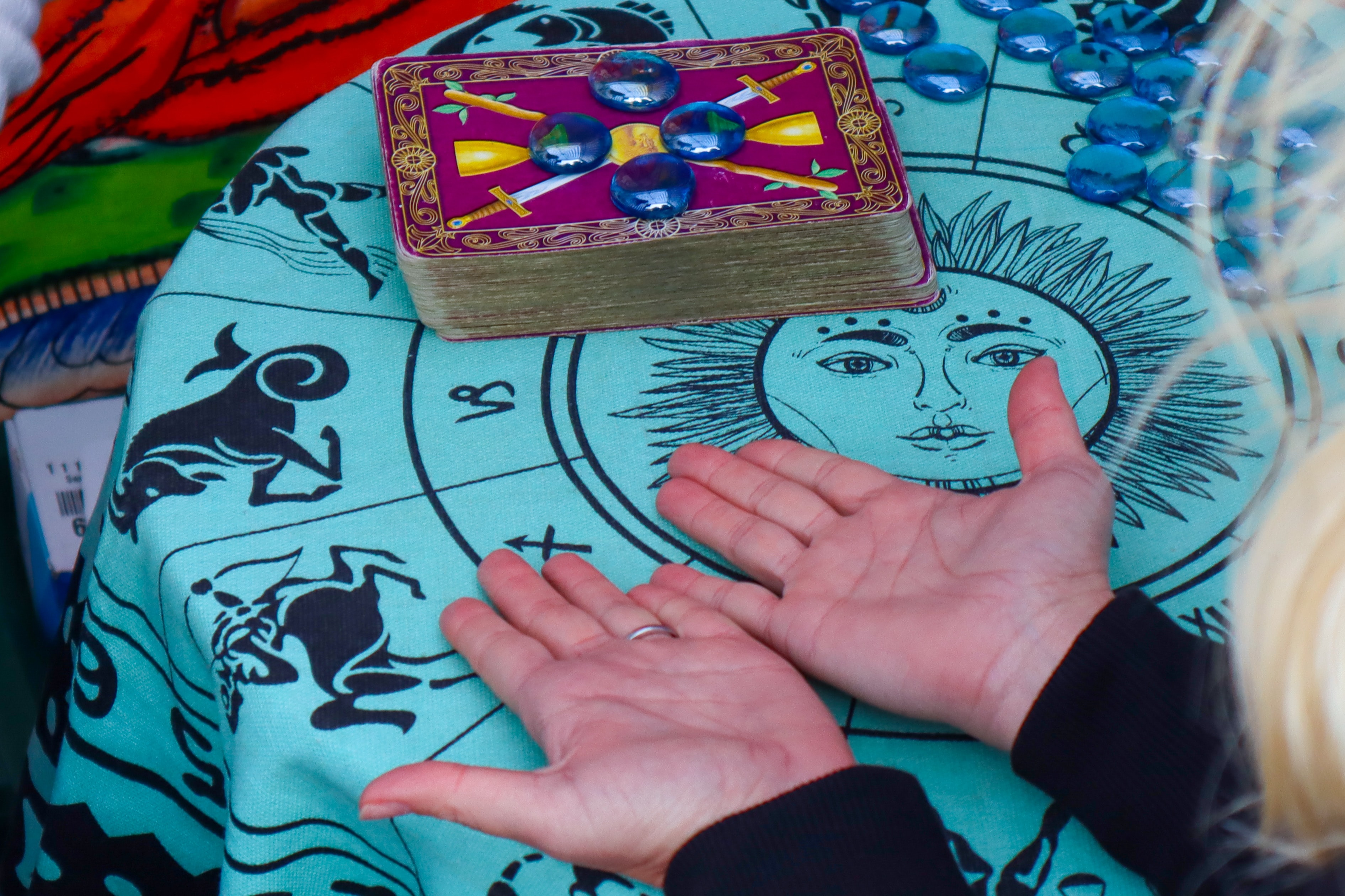 A person places their hands, palms up, on a table printed with zodiac signs.