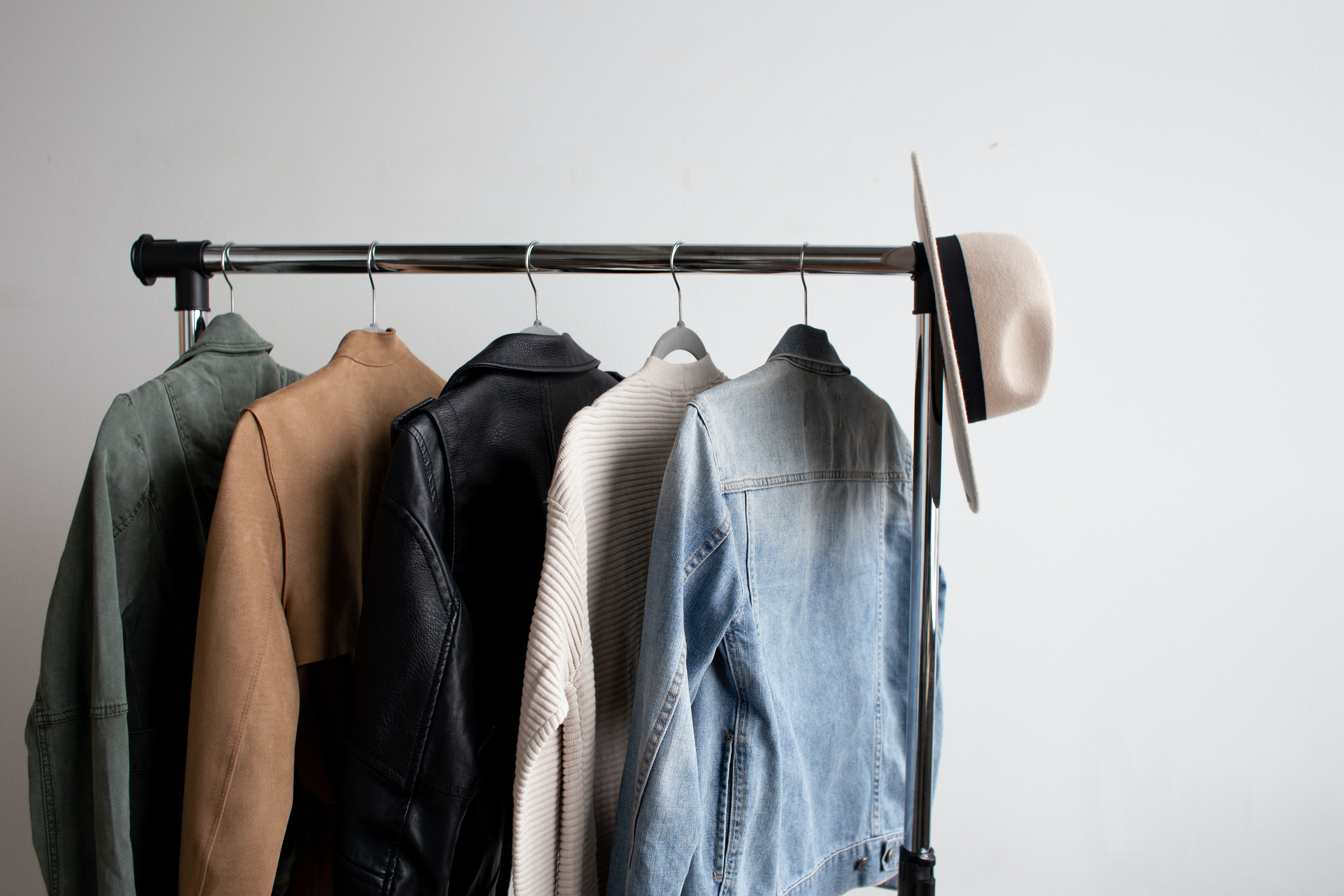 Five jackets and a hat hang on a clothing rack.