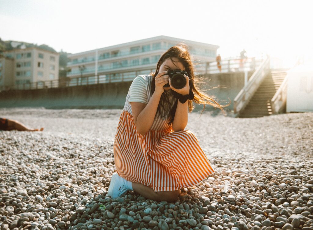 A woman in a striped dress kneels to take a photo with a professional camera. 