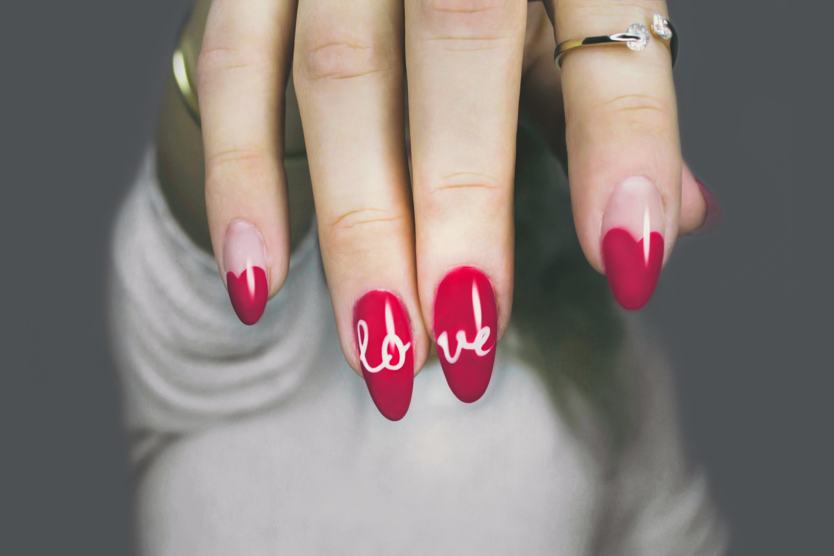 A woman holds her hand up to the camera, showing off red nails with "love" written on them.