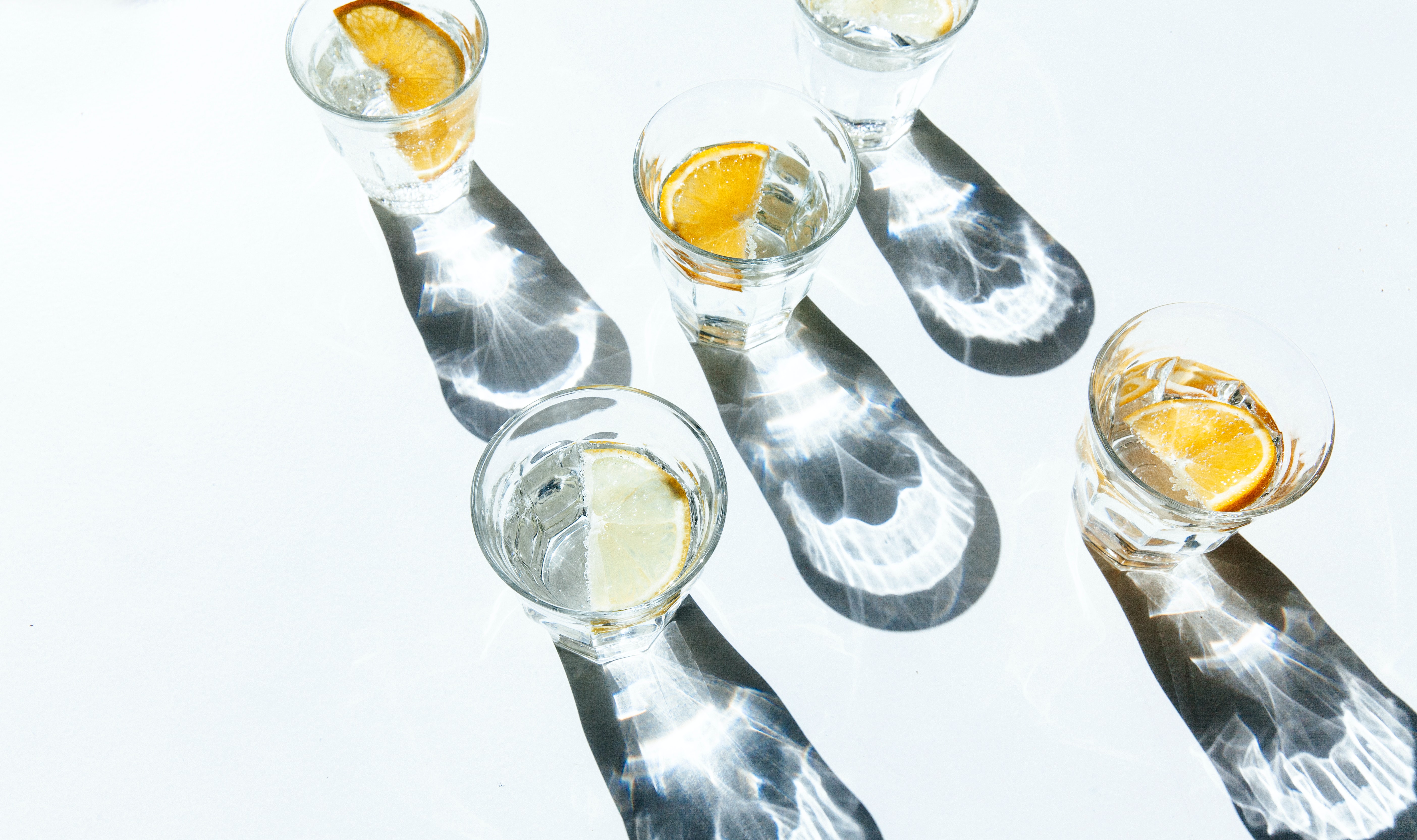 Five shot glasses filled with clear liquid and orange slices.