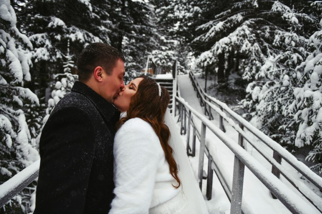 A bride and groom kiss in a snowy forest.