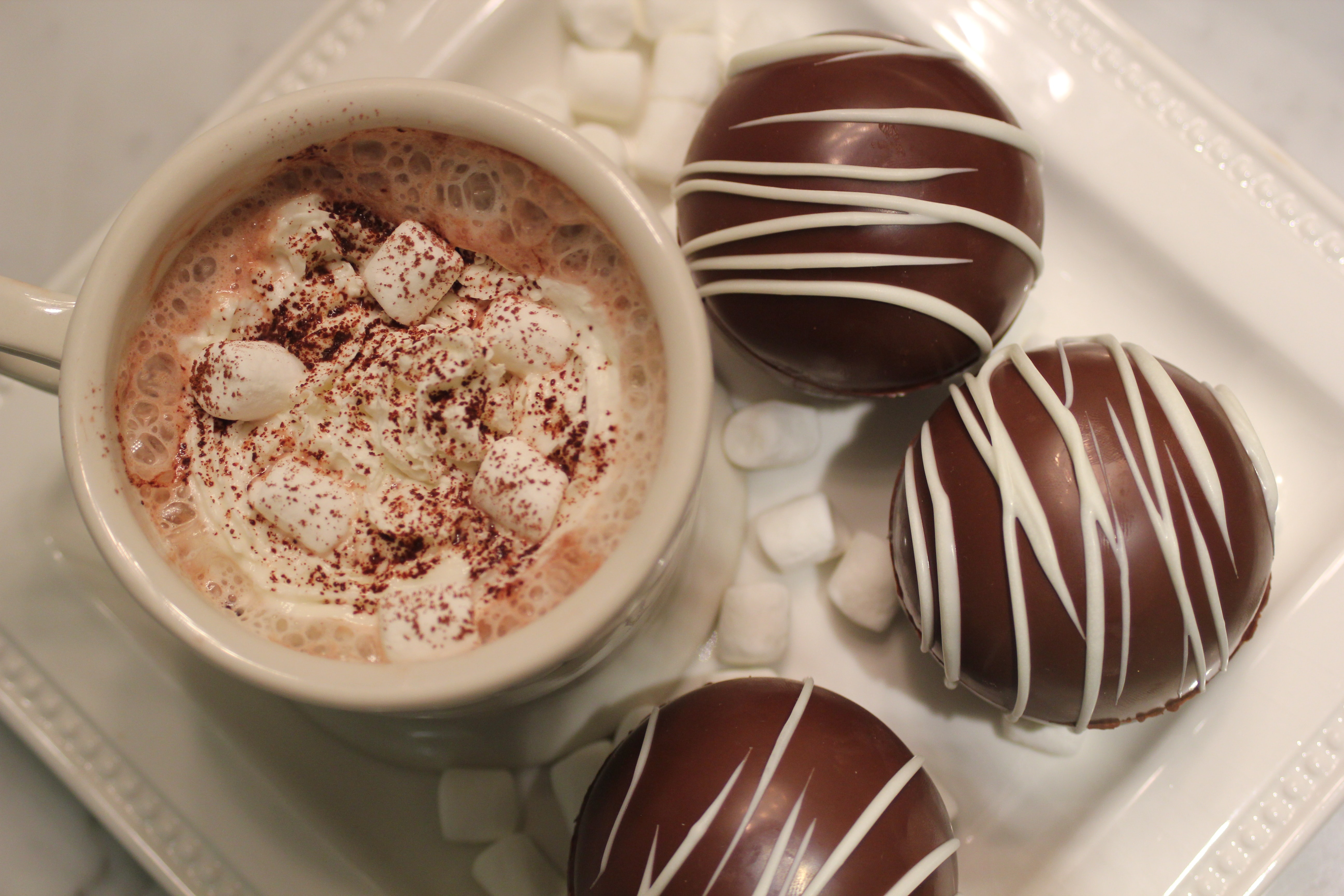 A cup of hot cholate with marshmallows on a tray with chocolate balls.