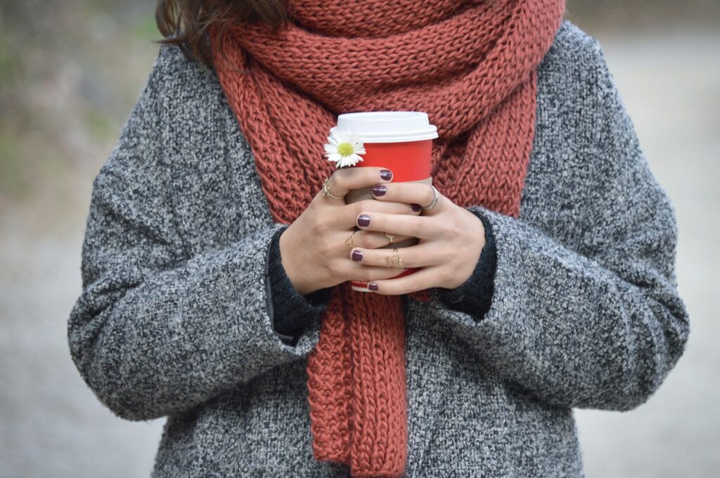 A woman wearing a scarf holding a cup of coffee. 