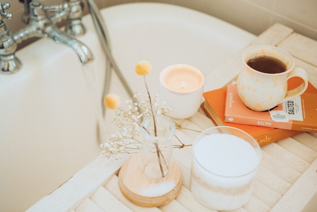 A tray with flowers, candles, books and a cup of tea sits across a bathtub.