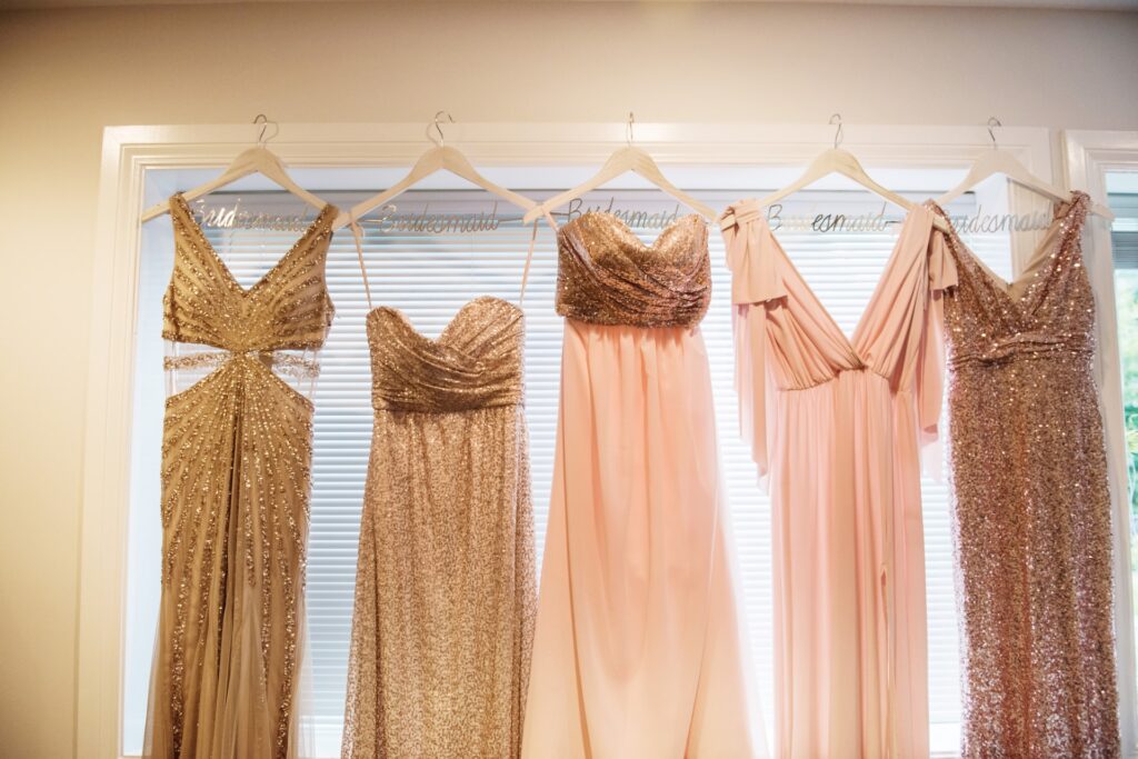 Pink and gold bridesmaid dresses hang on hangers.