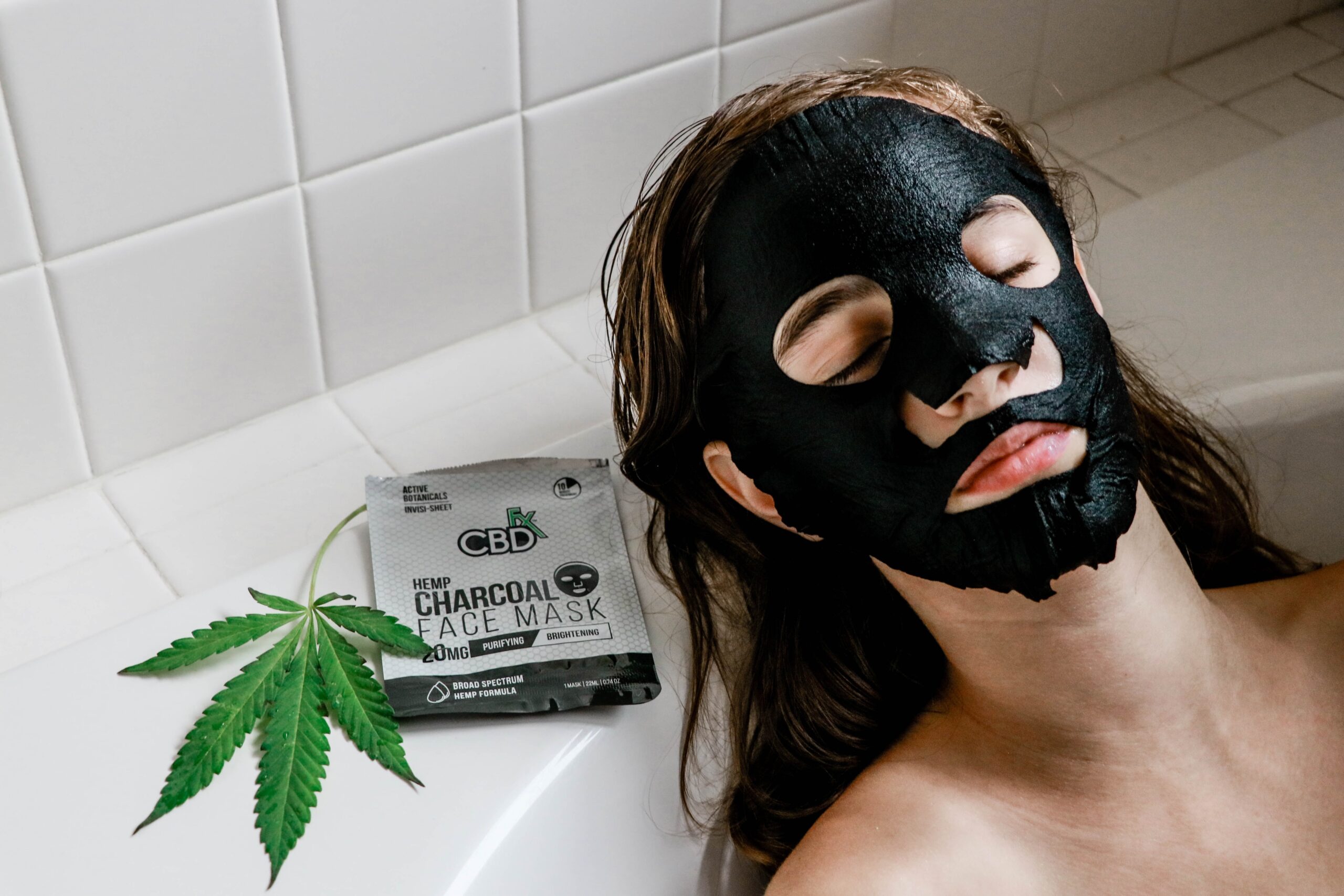 A woman lies in a bathtub with a black charcoal mask on her face.