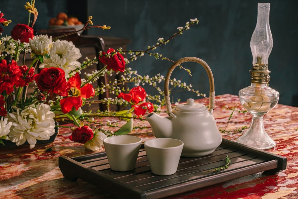 A tea tray sits on a table next to a red and white floral arrangement.